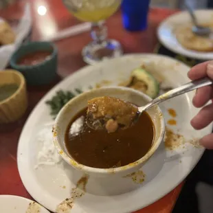 a hand holding a spoon over a bowl of soup