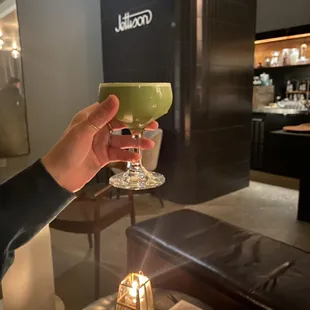 a person holding a glass of green liquid