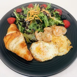 a plate of food with a croissant, salad, and shrimp
