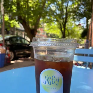 Large iced coffee. Shaded outdoor seating in the middle of the day.