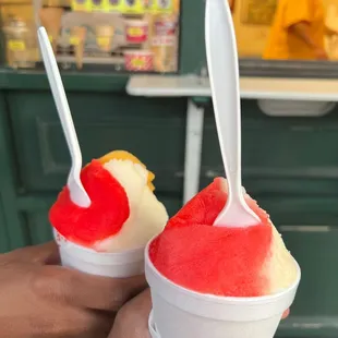 ows a hand holding two cups of ice cream