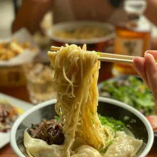 a person holding chopsticks over a bowl of ramen