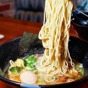 a bowl of ramen noodles being lifted by a pair of chopsticks