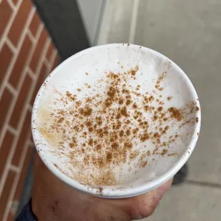 a hand holding a cup of cappuccino