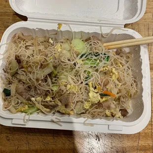 a take out container of noodles with chopsticks