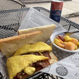 Breakfast sandwich with scrambled eggs and bacon with fresh fruit. San Pellegrino sparkling water.