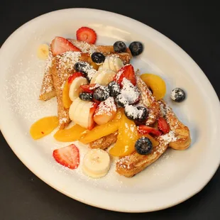 a plate of french toast with fruit and powdered sugar