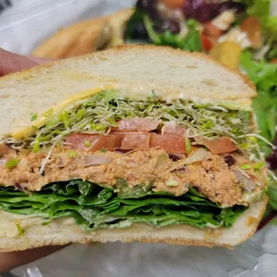 a hand holding a sandwich with lettuce and tomatoes