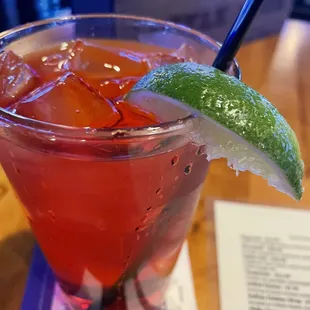 a red drink with a lime garnish
