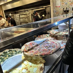 a woman standing in front of a counter full of pizzas