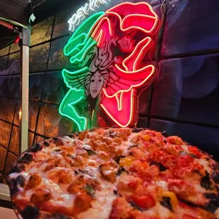 a pizza on a plate in front of a neon sign