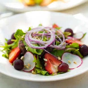 Salad bowl of mix greens with grapes, strawberries, shaved red onion,radishes, sunflower seeds, goat cheese, and honey balsamic vinaigrette