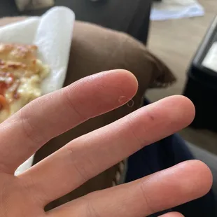 a person's hand with a piece of pizza in the background