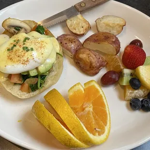 a plate of eggs benedicts, fruit, and potatoes