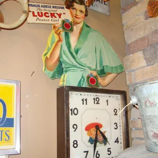 A Buster Brown wall clock and a large cardboard Lucky Cigarettes ad from the 1930s.