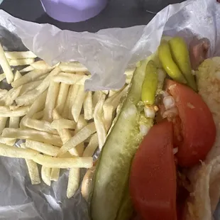 Fraser, pale, tomatoes, and pickles are way too big, twice as wide as the hotdog and the peppers are thrown on willy-nilly