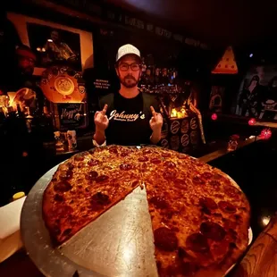 a man standing behind a large pizza