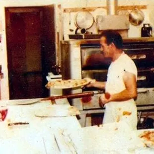 a man holding a pizza in a kitchen