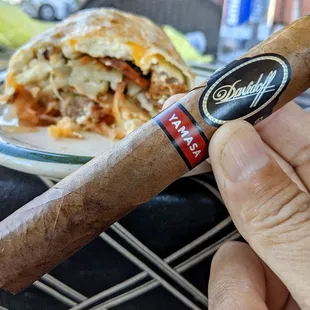 a hand holding a cigar and a plate of food