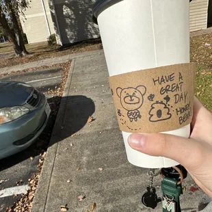 a hand holding a coffee cup with a drawing on it