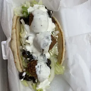 Falafel Sandwich with sauce, lettuce, tomato, cucumber, and olives.