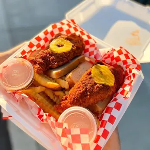a hand holding a basket of fried chicken and fries