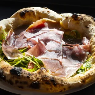 a pizza with ham and greens