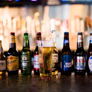 a variety of beer bottles lined up on a bar counter
