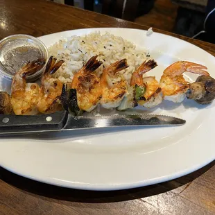 Shrimp kabob with large grilled shrimp, seasoned rice and a side salad.