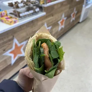 a person holding a sandwich in a paper wrapper