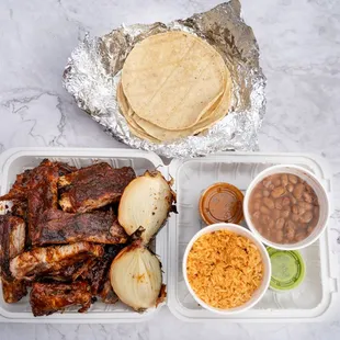 a plate of ribs, beans, rice, and tortillas