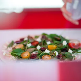 The Grecian: a white pie with Baby Spinach, Heirloom Cherry tomatoes, Kalamata Olives, Mozz/Provolone Cheese, Greek Isles Feta Cheese.