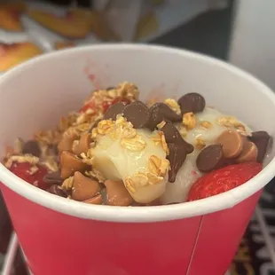Frozen yogurt with a spoon full of chocolate chips and 1 strawberry sliced up