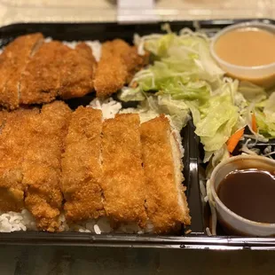 a meal of fried chicken, rice, salad, and dipping sauce