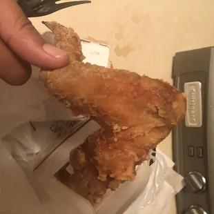 a hand holding a piece of fried chicken