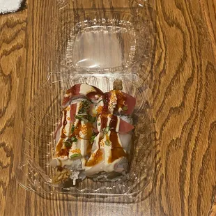 a plastic container of sushi on a wooden table