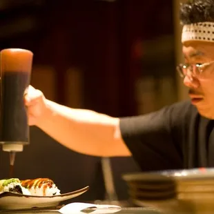 Another sushi chef putting on sauce.