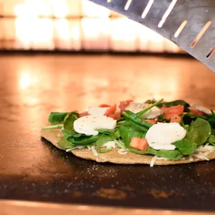 a pizza with spinach, tomatoes, mozzarella, and mozzarella cheese