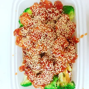 a container of food with sesame seeds and broccoli
