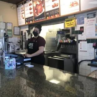 a woman in a mask behind the counter of a restaurant