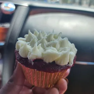 a hand holding a red velvet cupcake