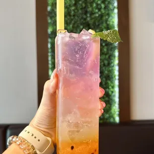 a hand holding a pink and yellow drink