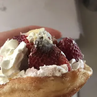 a hand holding a donut with whipped cream and strawberries