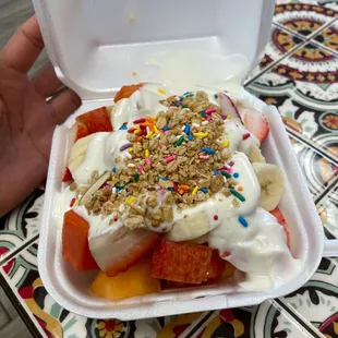 a hand holding a container of fruit and yogurt