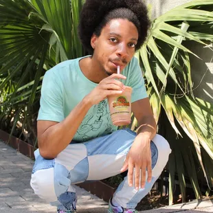 a young man sitting on the ground with a drink in his hand