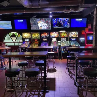 a row of bar stools in front of a row of televisions