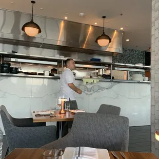 White coat man had a cough but stands at the window facing the food inches away from plates.