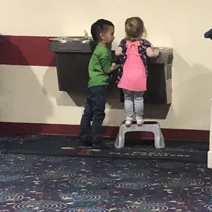 A little gentlemen holds the button for the little girl to get a drink