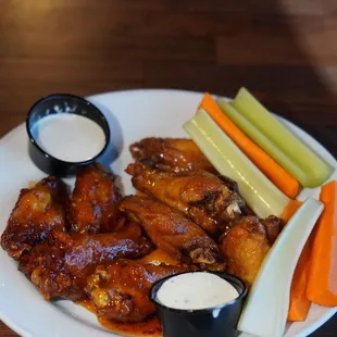 a plate of chicken wings, carrots, celery, celery sticks, and dips