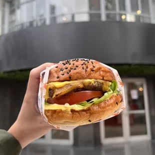 a person holding a hamburger in front of a building